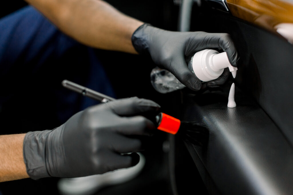 Cropped close up shot of hands of African male auto detailing workshop, wearing protective gloves, holding soft brush and applying cleansing foam on the surface of vehicle door.