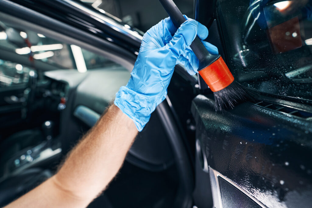 Auto mechanic dry-cleaning door of car under window with brush and cleaner