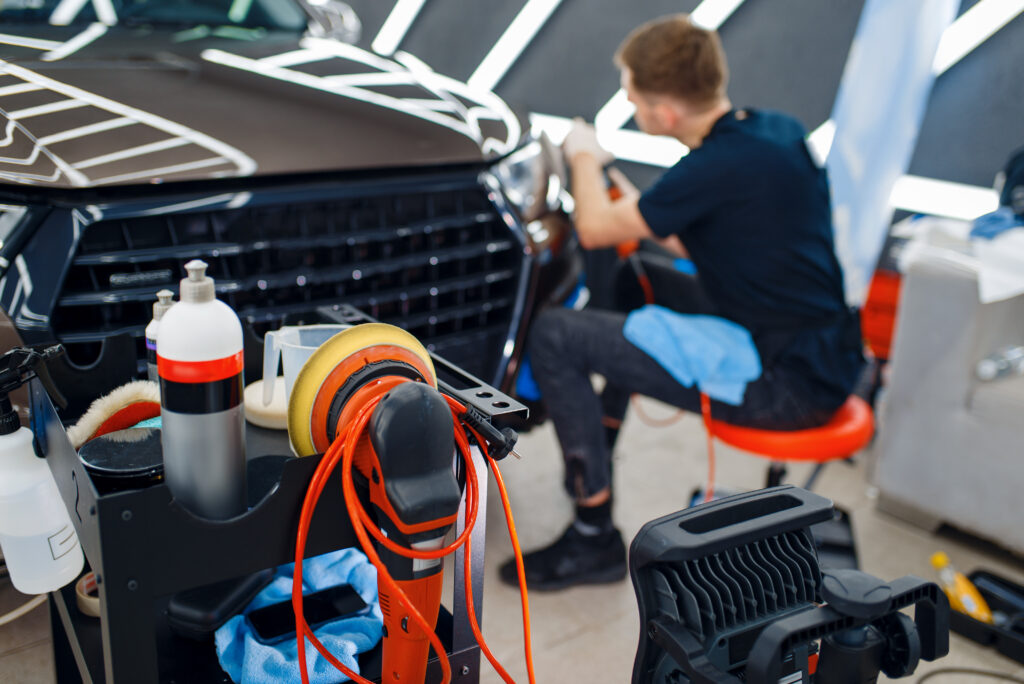Male worker polishes headlights using polishing machine, car detailing. Preparationa before installation of coating that protects the paint of automobile from scratches. Auto tuning in workshop